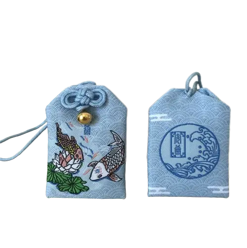 Breloque japonaise omamori avec des motifs de poissons koï et de fleurs de lotus sur un tissu bleu clair.