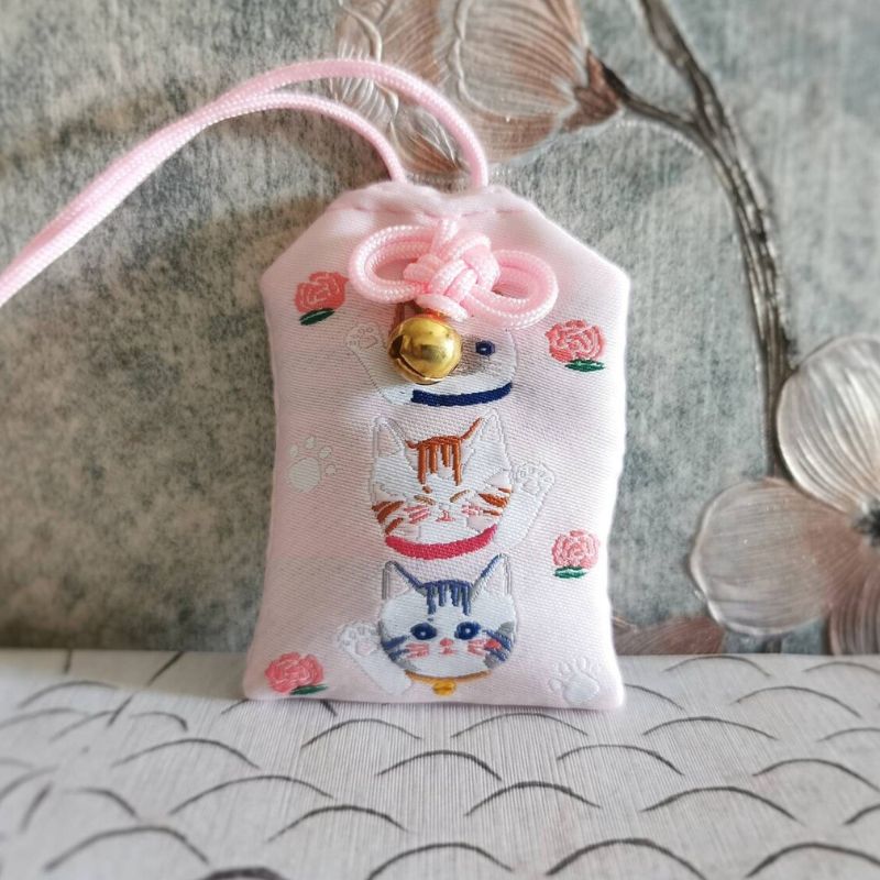 Breloque ou pochette en tissu rose décorée de chats et de motifs floraux, avec une petite clochette dorée.