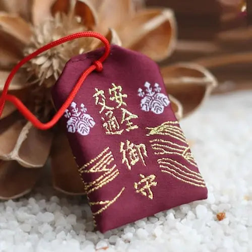 Breloque omamori violette avec caractères japonais dorés et cordon rouge.