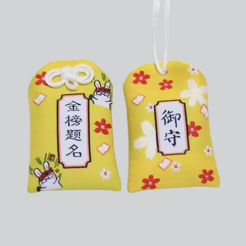 Deux omamori (porte-bonheur) japonais jaunes décorés de fleurs de cerisier et de caractères kanji.