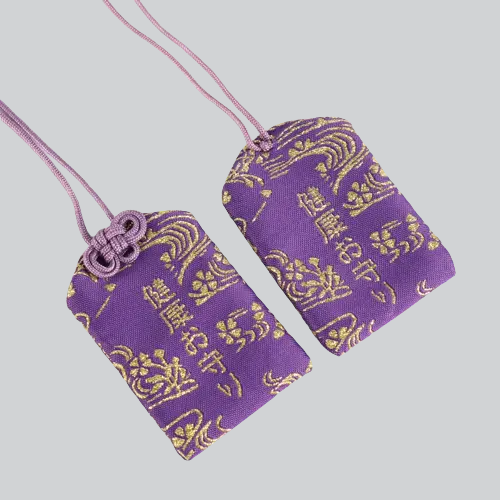 Deux pochettes d’amulettes en tissu violet avec des motifs décoratifs dorés et des cordons roses.