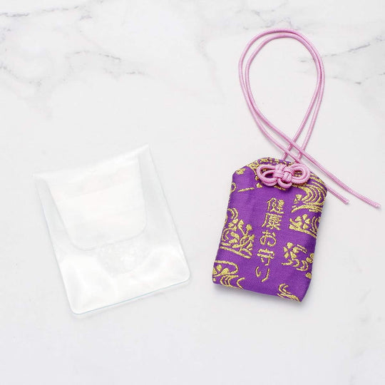 Breloque omamori en tissu violet et doré avec un cordon rose.