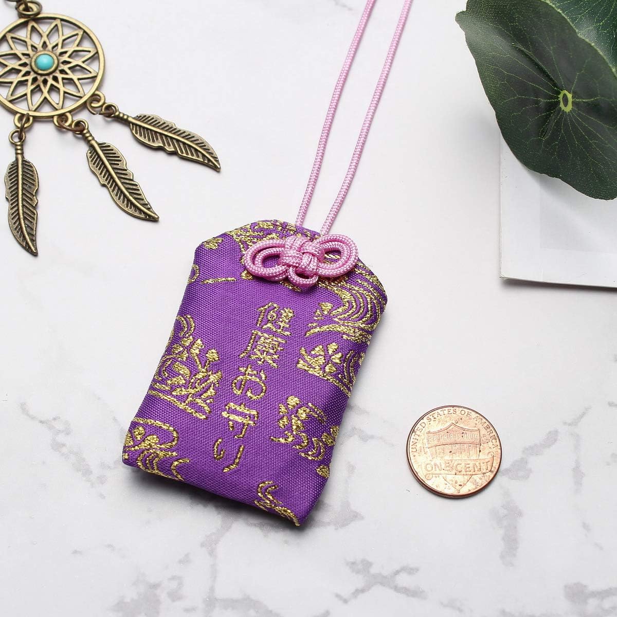 Breloque omamori en brocart violet avec des motifs dorés et un nœud rose.