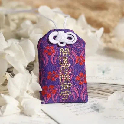 Breloque japonaise omamori avec tissu de brocart violet et rouge et caractères dorés.