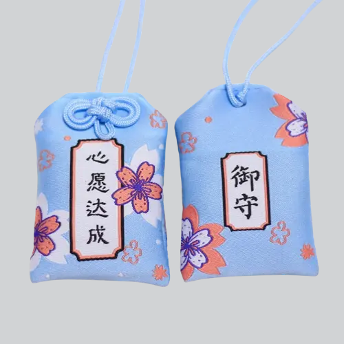 Deux omamori (pochettes à breloques) japonais bleu clair décorés de fleurs de cerisier et de caractères kanji.