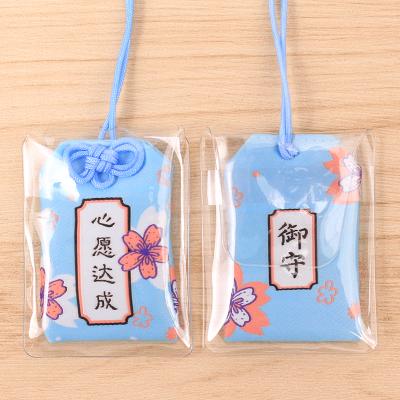 Deux omamori (amulettes protectrices) japonaises bleues avec des motifs de fleurs de cerisier et des caractères kanji dans des pochettes en plastique.