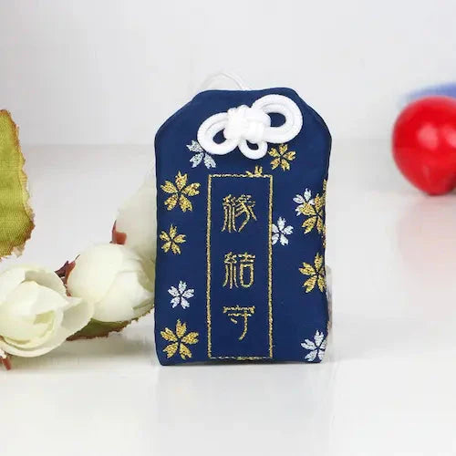 Breloque japonaise omamori bleu marine décorée de fleurs de cerisier dorées et argentées.