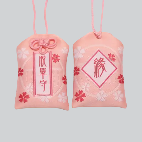 Deux omamori (porte-bonheur) japonais roses avec des motifs de fleurs de cerisier et des caractères kanji.