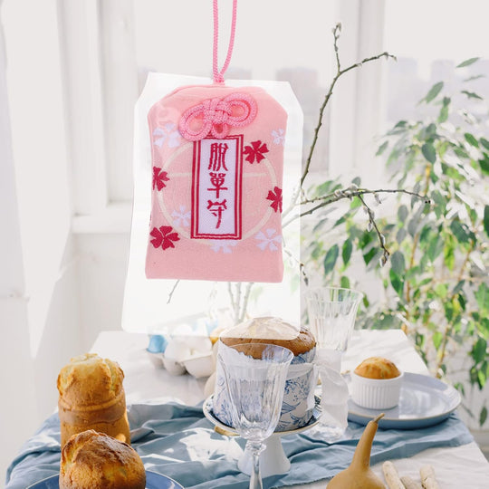 Breloque japonaise omamori rose avec décorations de fleurs de cerisier et caractères kanji.